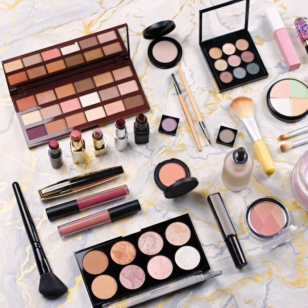 Maquiagem completa com paletas de sombra, batons, blush e pinceis dispostos sobre uma superfície de mármore. Perfeito para criar looks elegantes e variados para diferentes ocasiões.